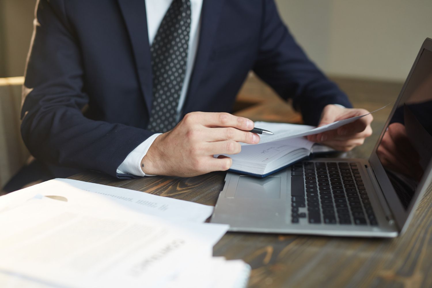 Businessperson reviewing documents beside a laptop at a desk