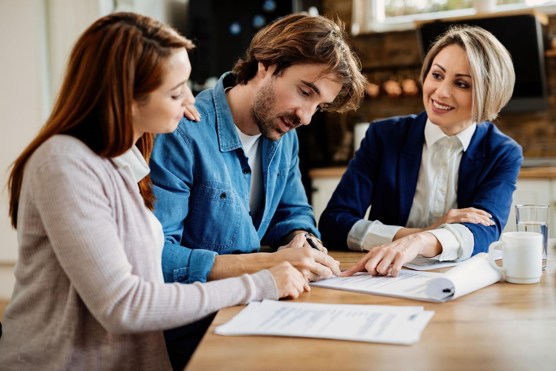 Three coworkers reviewing documents and smiling at a table in a bright office