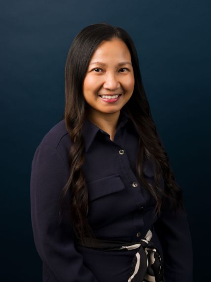 Smiling person in a dark jacket against a blue backdrop