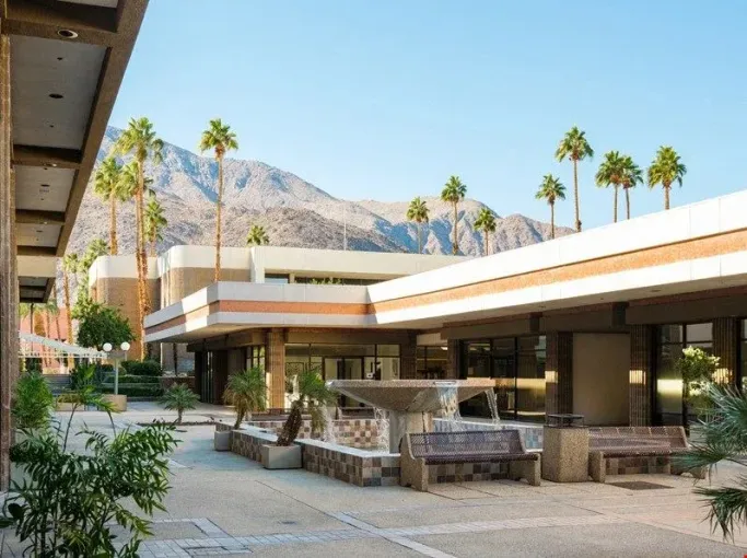Modern desert resort courtyard with palm trees, lounge seating, and mountains in the background