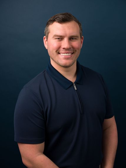 Smiling man in a navy shirt posing against a dark blue background