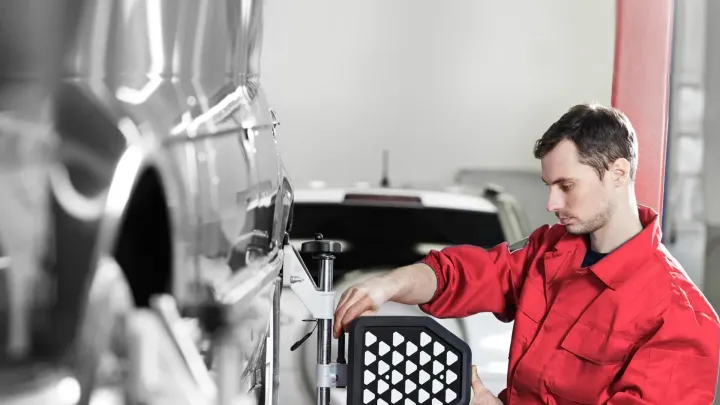 A man in a red uniform is working on a car in a garage. A man in a red uniform is working on a car in a garage.