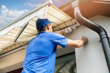 A man in blue workwear is installing or repairing an awning near a gutter.