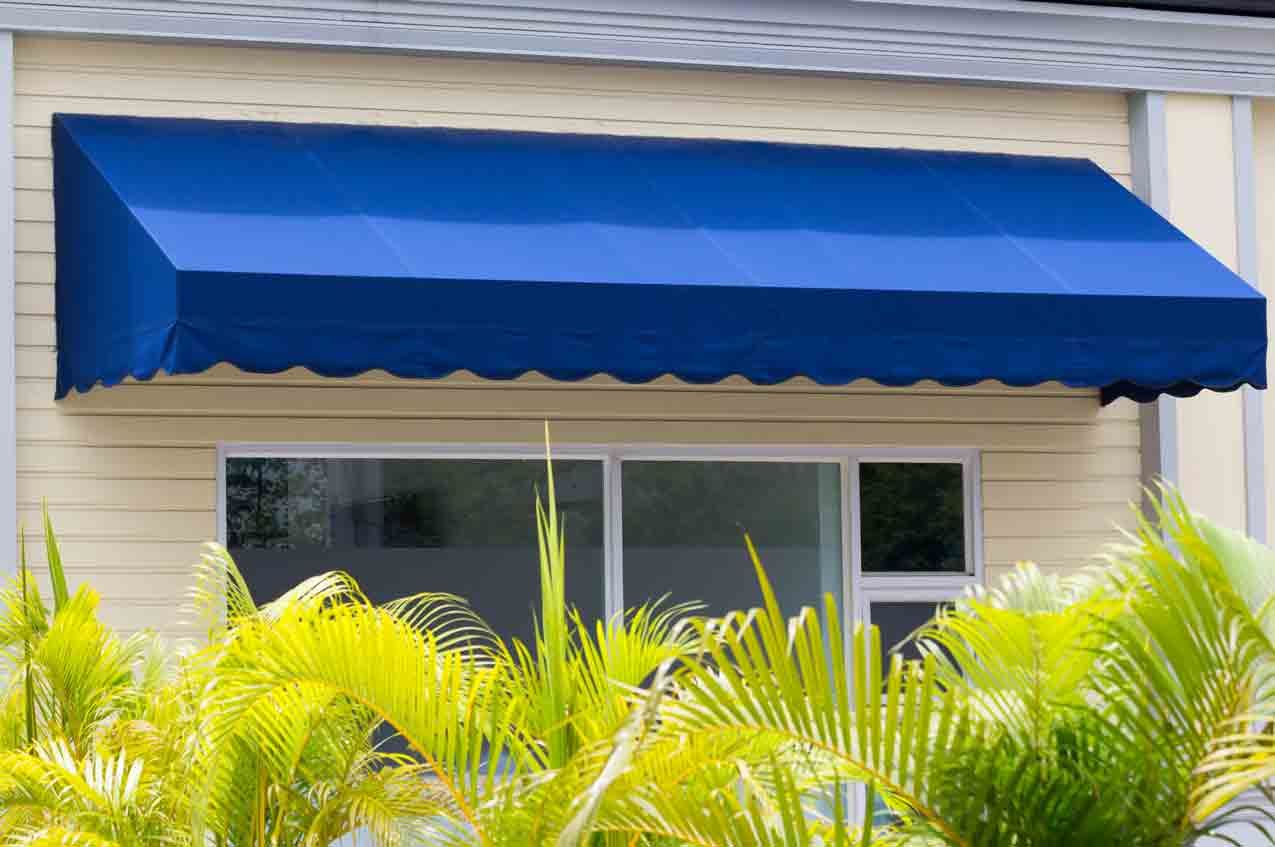 Blue awning over a window, yellow siding, with green plants in the foreground.