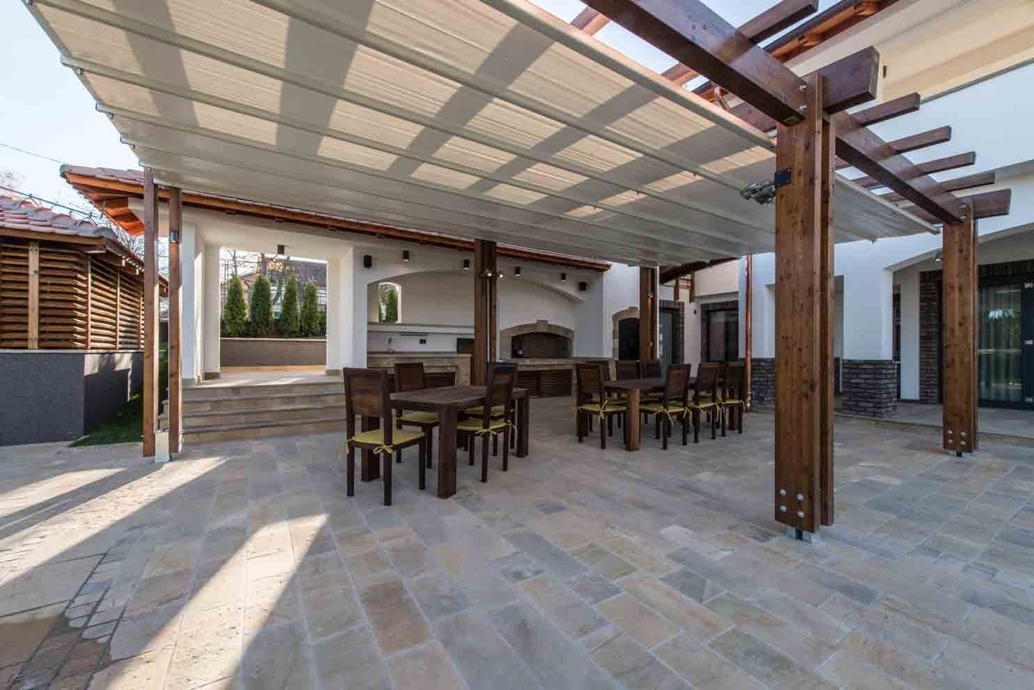 Outdoor patio with wooden pergola, tables, chairs, and a built-in grill.