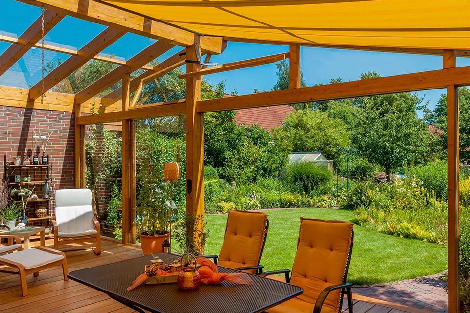 Patio with yellow shade, wooden beams, furniture, and a view of a lush green yard.
