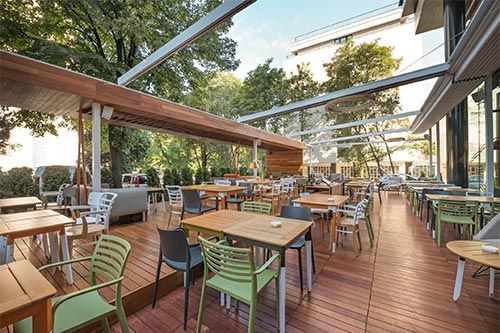 Outdoor restaurant seating area with wooden deck, tables, and colorful chairs under a canopy.