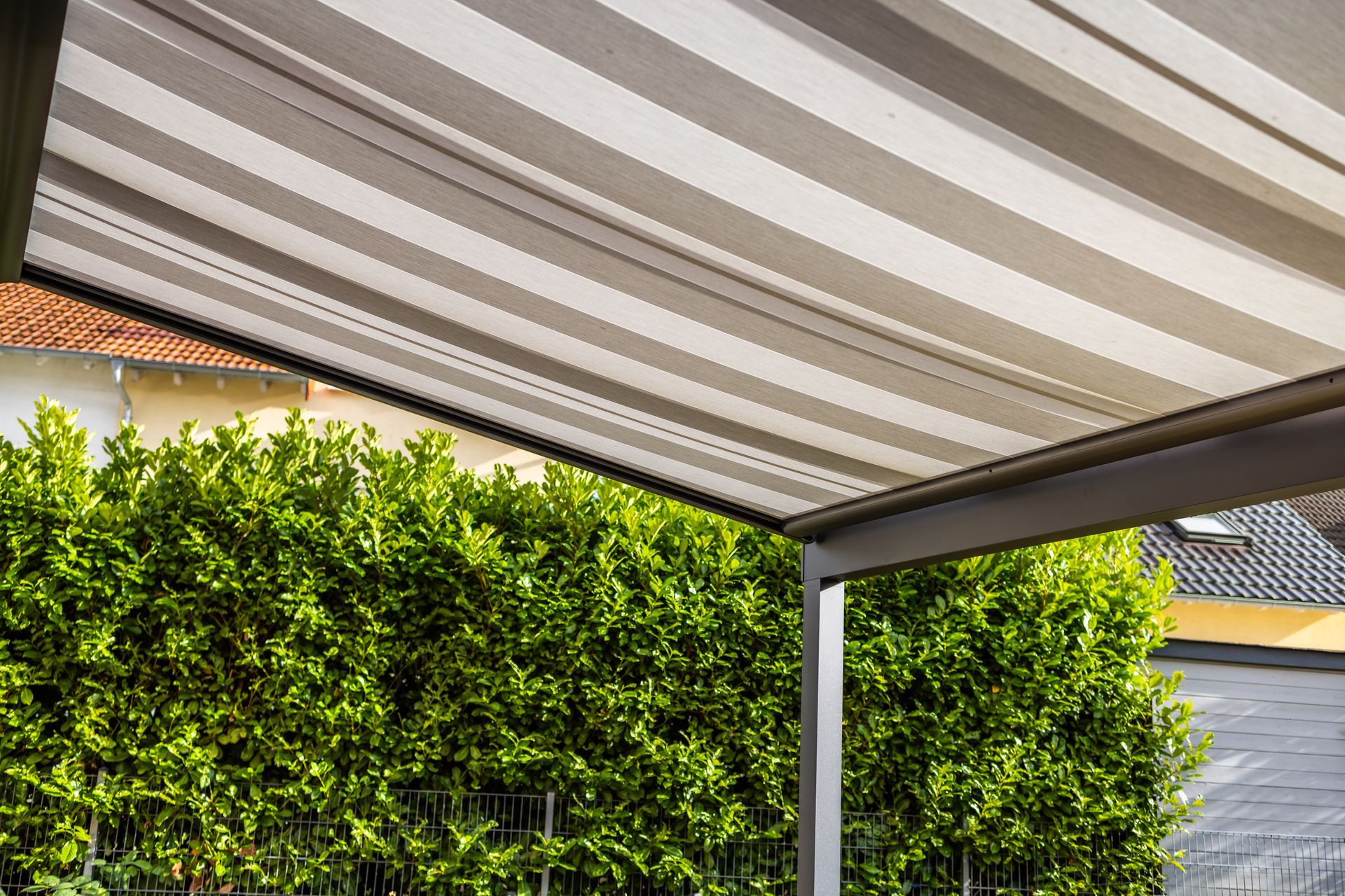 A striped patio awning extending over a backyard garden, providing shade above an outdoor seating
