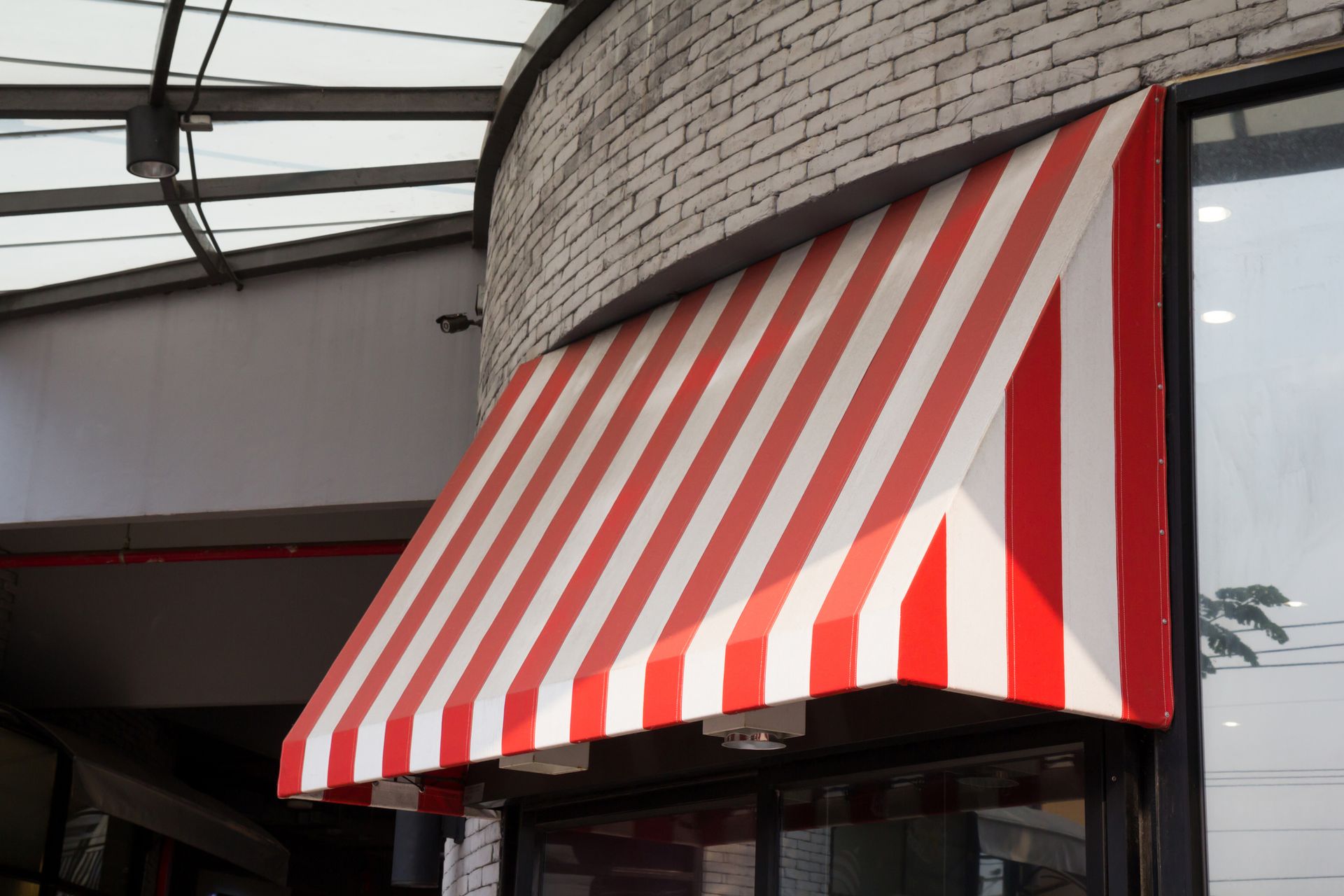 Red and white striped storefront awning on brick building under glass canopy entrance exterior view.