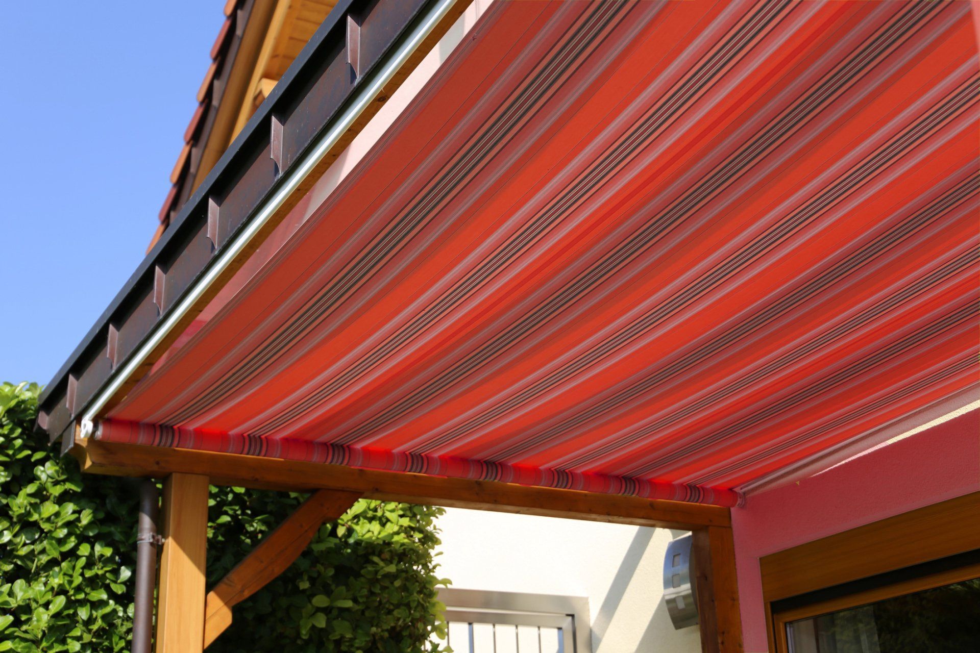 Red and white striped awning covering a wooden patio; sunny outdoors.