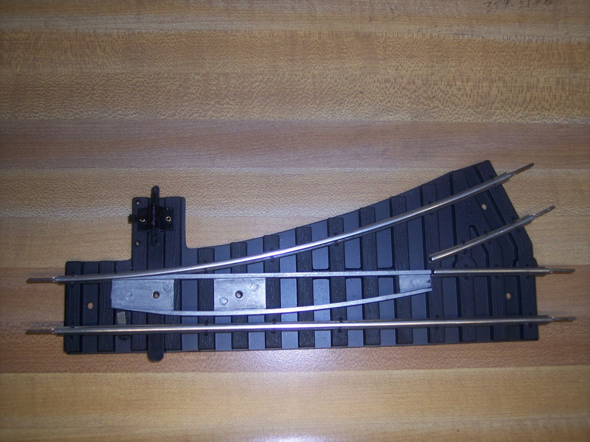 Model train track turnout switch on a wooden surface, with black rails and a curved diverging route
