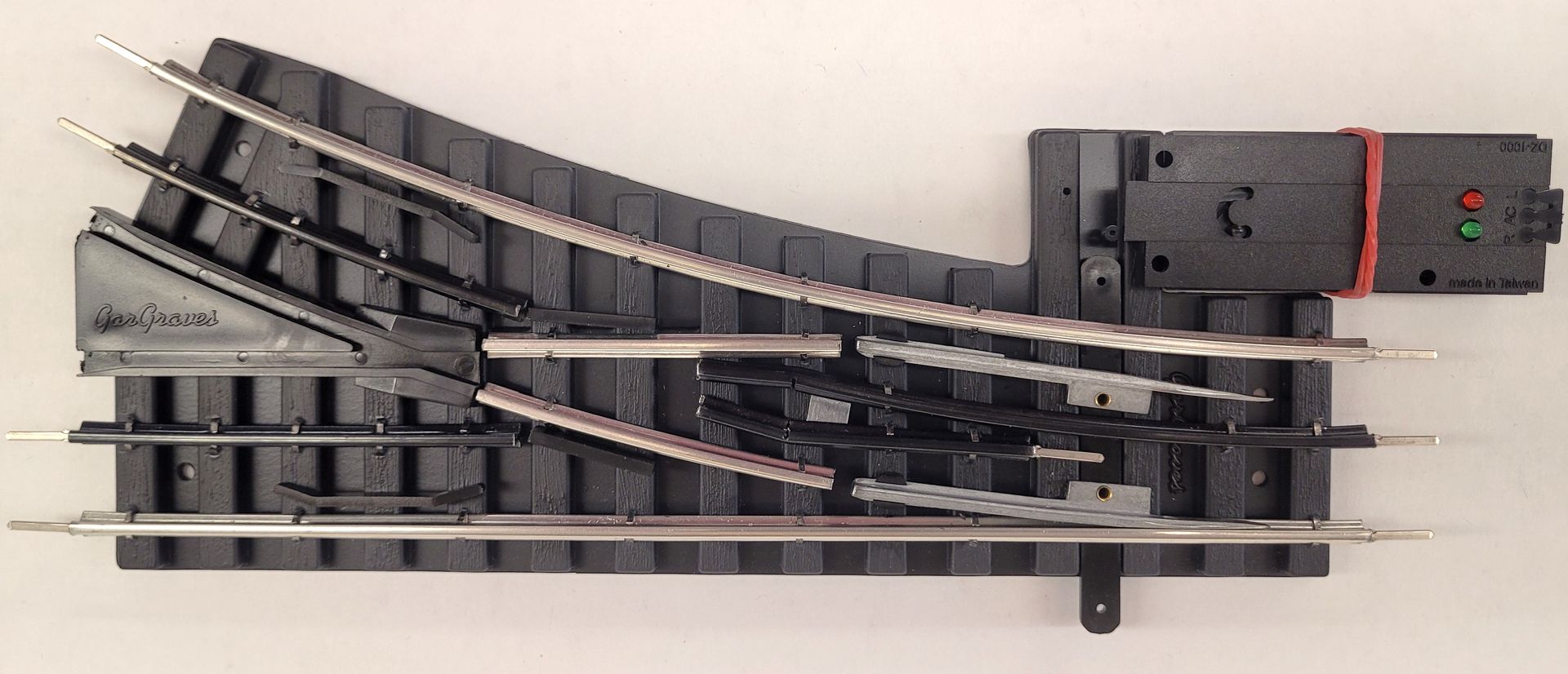 Toy train tracks and switches arranged on a white surface, with a red control box on the right