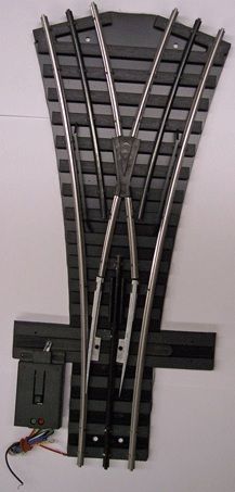 Model railroad turnout switch with black rails and a gray motor actuator attached on the left