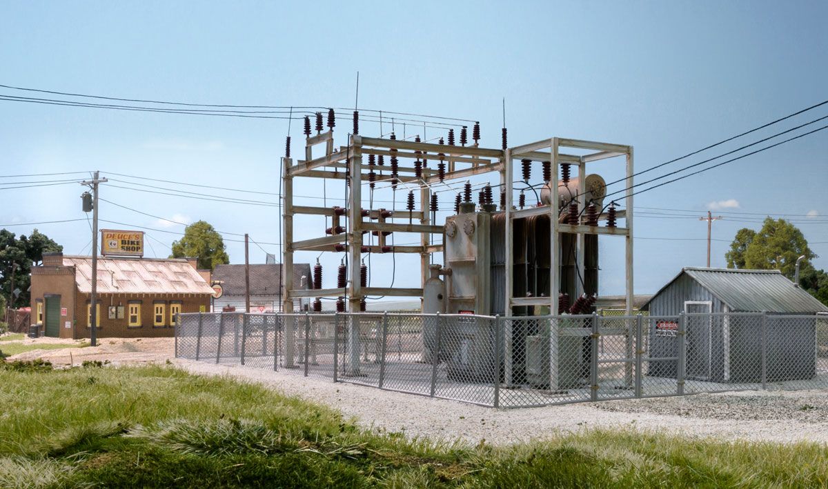 Electrical substation with metal framework, transformers, and power lines on a gravel lot under a clear sky