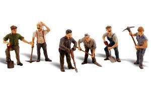 Five toy construction workers with tools standing in a row on a white background