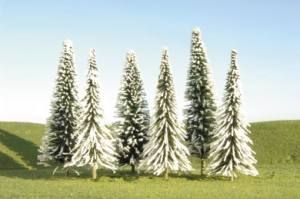 Snow-covered evergreen trees in a grassy field under a pale sky