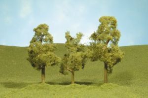 Three small trees on a grassy hill under a pale blue sky.
