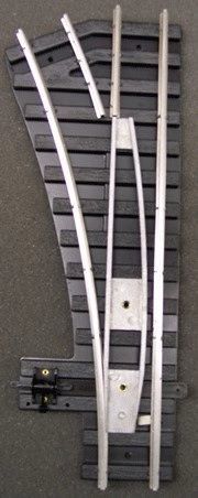 Curved white and black metal track switch mechanism mounted on a gray surface