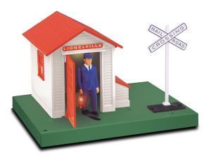 Toy train station with a blue-uniformed conductor standing in the doorway and a railroad crossing sign nearby