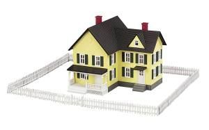 Yellow house model with black roof and white picket fence on a white background