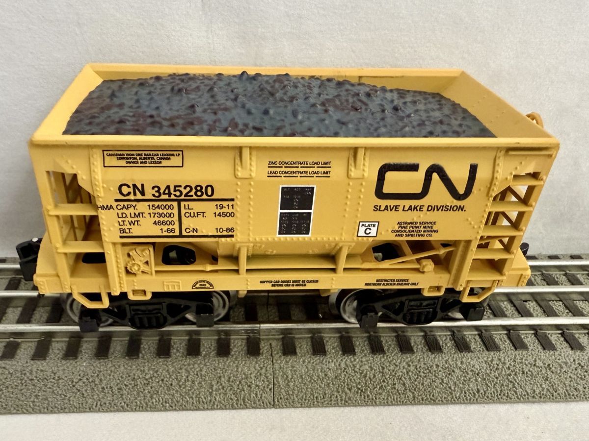 Yellow CN freight hopper car loaded with dark coal on model train tracks