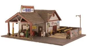 Miniature rustic gas station model with a small building, pumps, and a paved forecourt