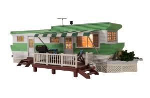 Green and white mobile home with porch and steps, shown in a side view.
