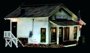 Miniature white post office model with a black roof, lit windows, and a U.S. flag at the entrance
