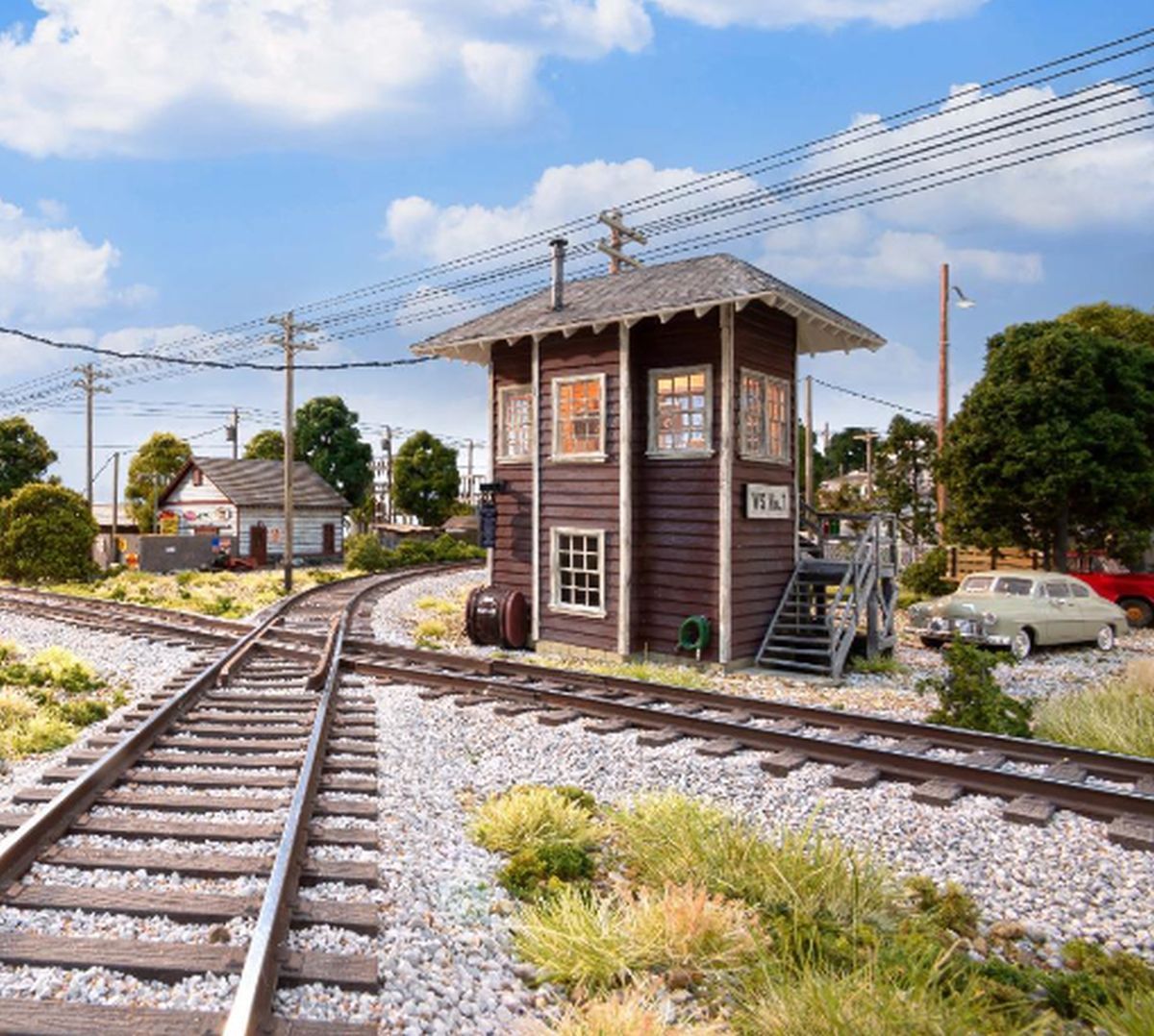 Railroad tracks crossing beside a small brown signal tower under a blue sky