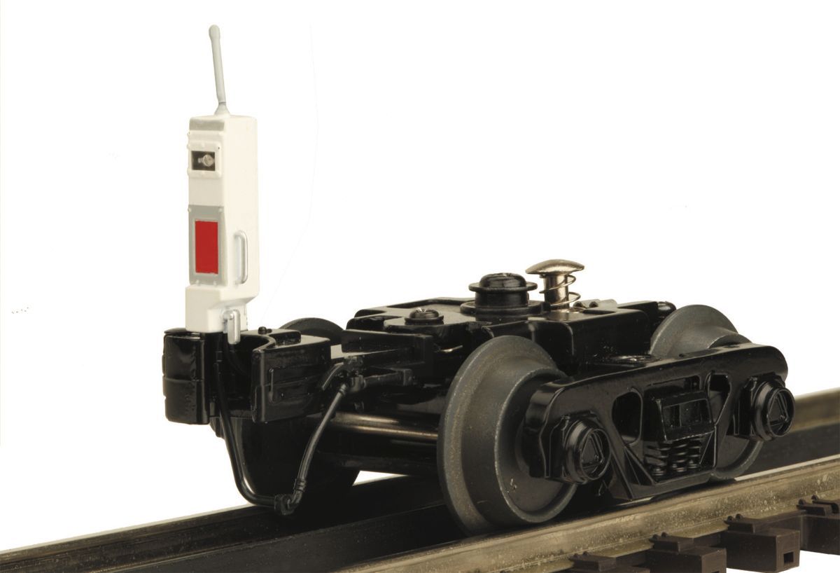 Black model train car with white-and-red device mounted on the front, sitting on a track