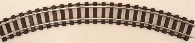 Curved miniature train track section with brown rails and black ties on a light background