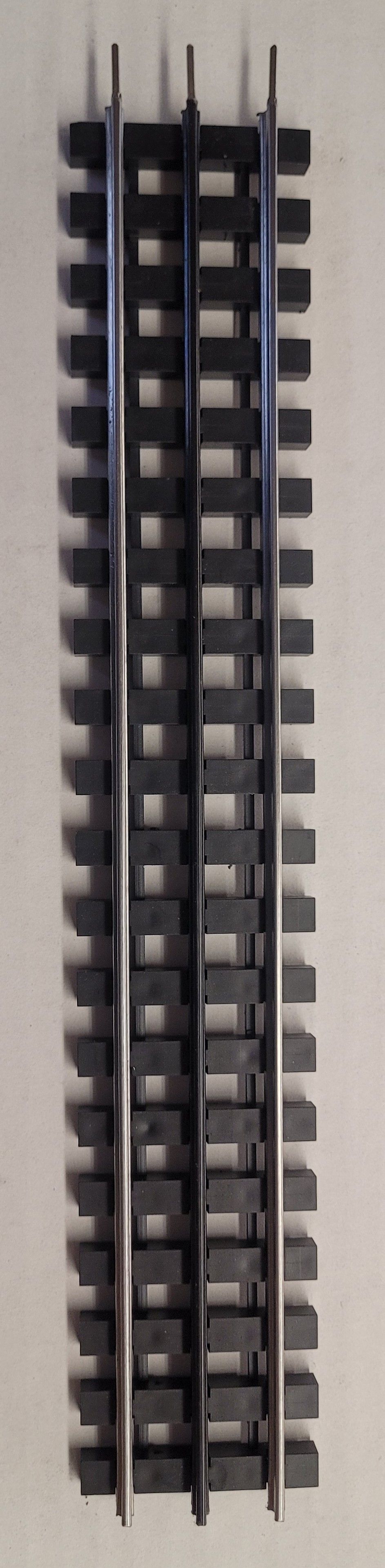 Close-up of a black plastic model train track section on a white background