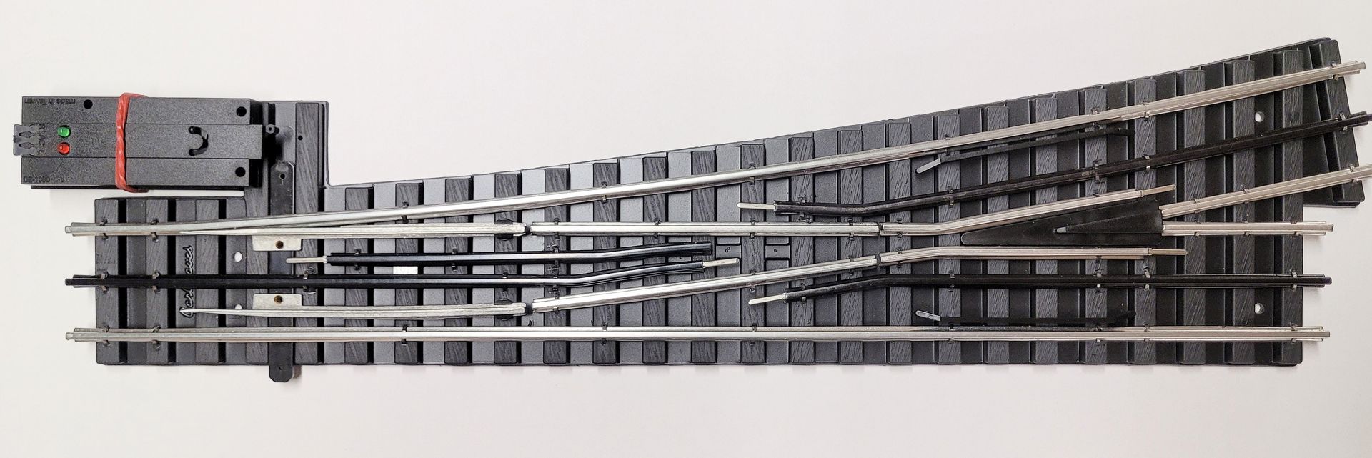Toy train track with a switch turnout, showing gray rails on a black base with a red control lever.