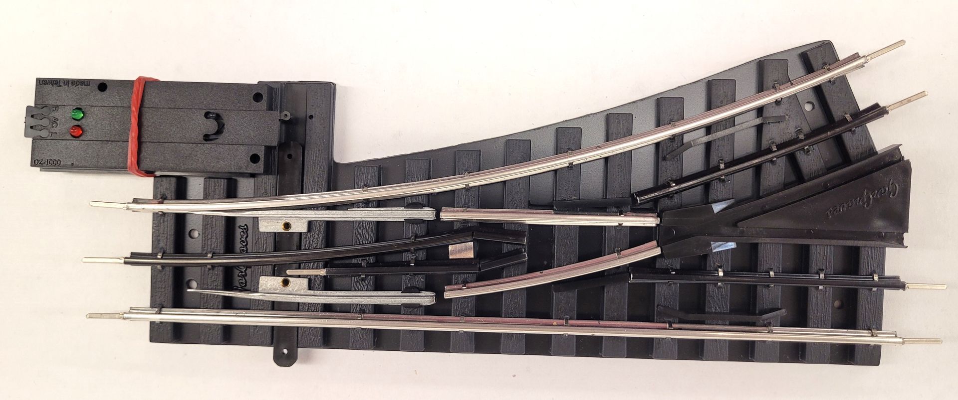Model train track switch with a curved section and black rails on a white background