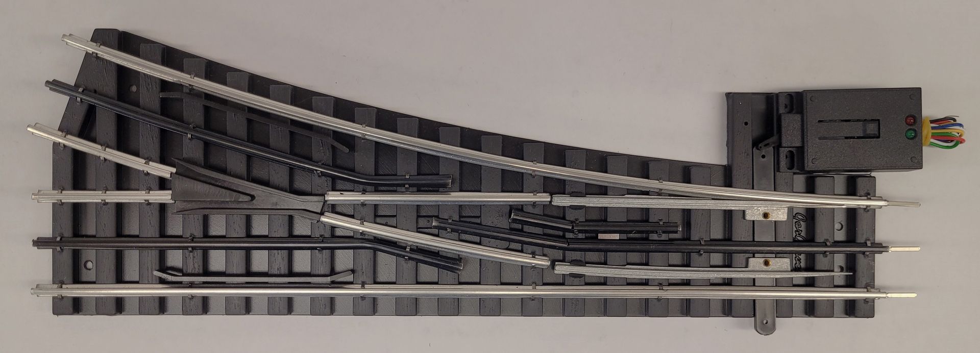Long gray model railroad track with multiple switches and a small control box on the right