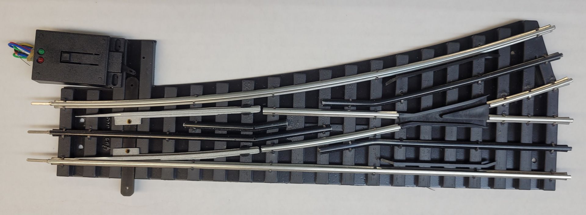 Black model train track switch with four curved rails on a white background