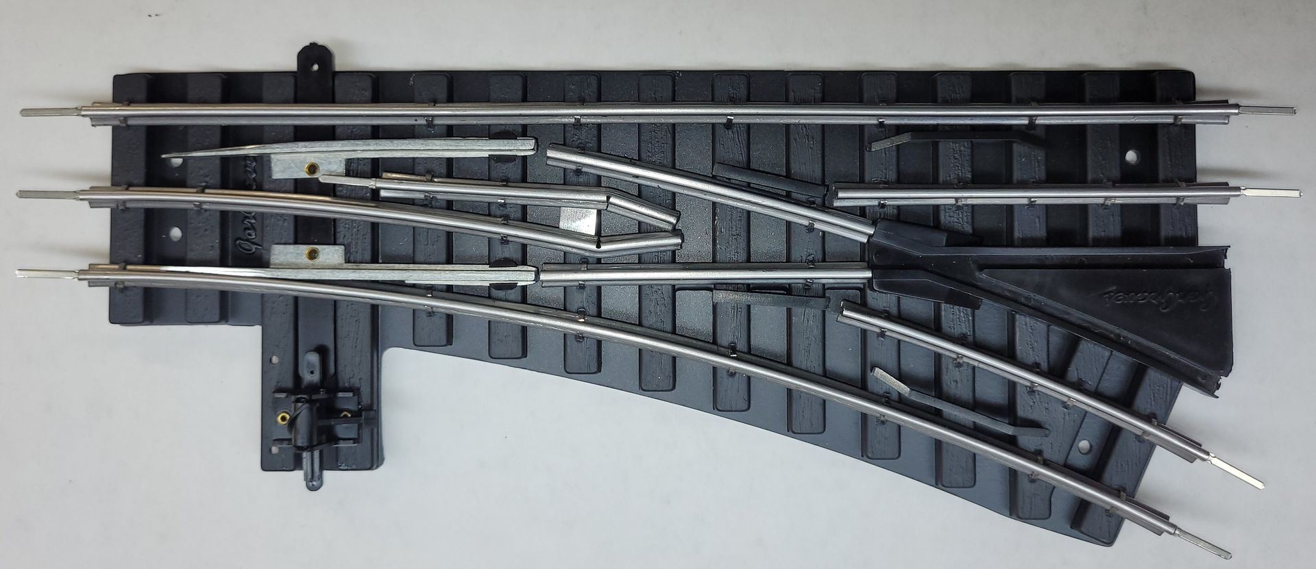 Overhead view of a model train track switch with curved and straight rails on a gray background