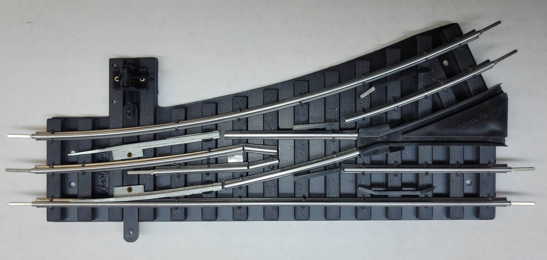 Curved model railway track switch, black plastic rails on a white background