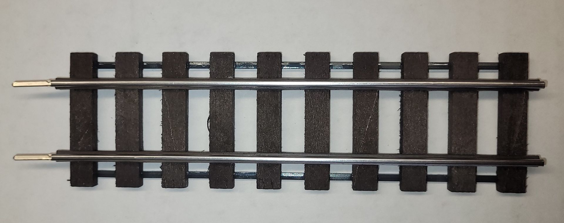 A short section of black model railroad track with metal rails on a light background