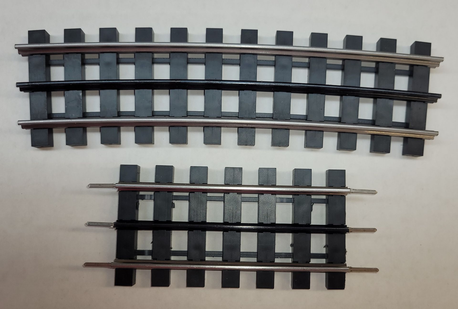 Two curved model train track sections, one above the other, on a light background
