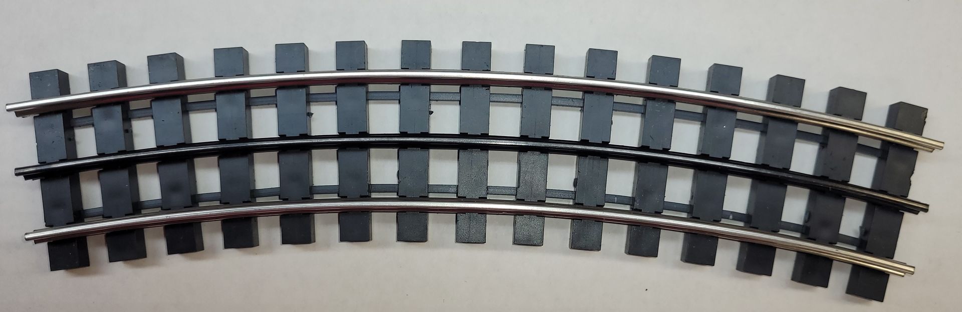 Curved section of model train track with gray ties and metal rails on a white background