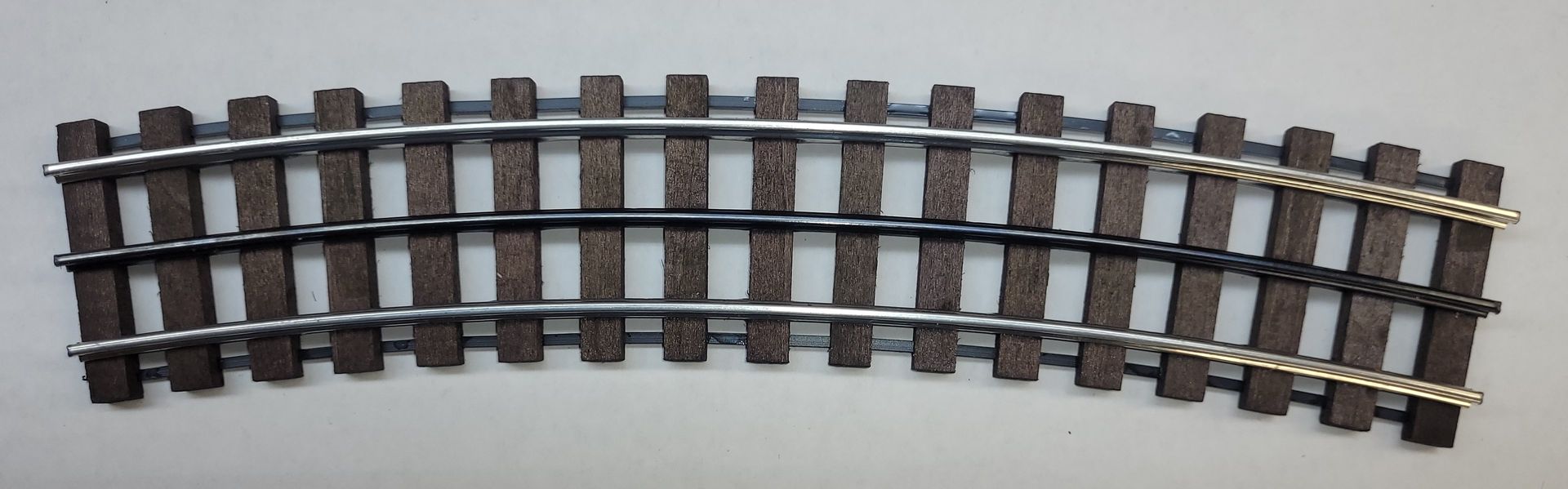 Curved section of metal model train track with brown wooden ties on a light background