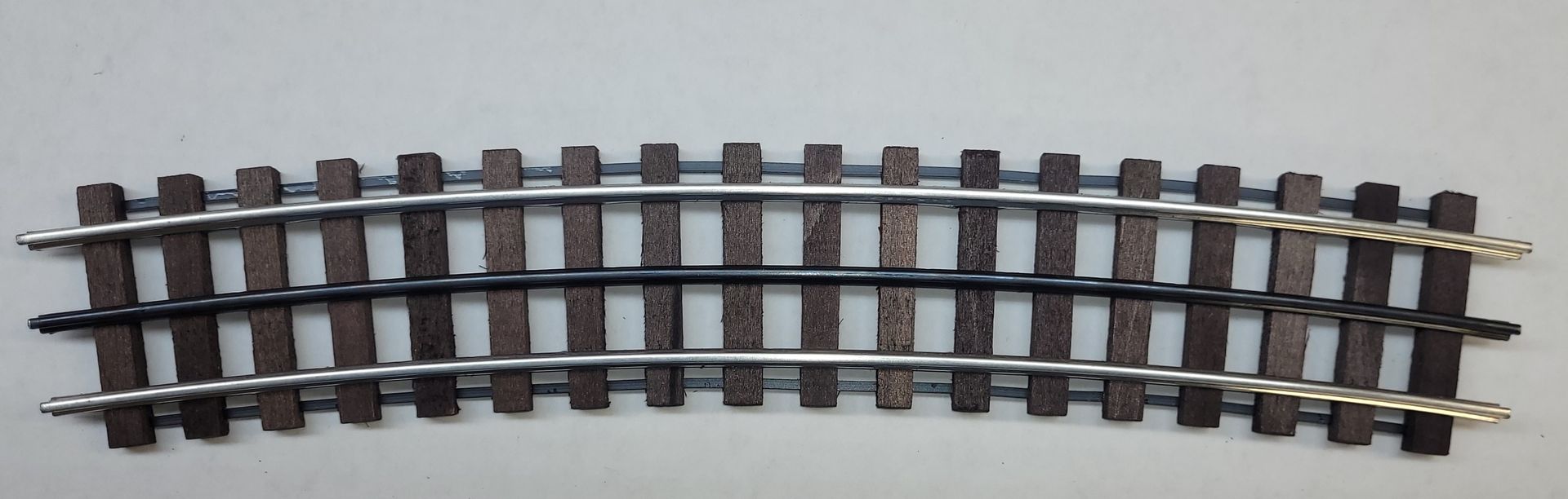 Curved model train track section with dark rails and gray ties on a light background
