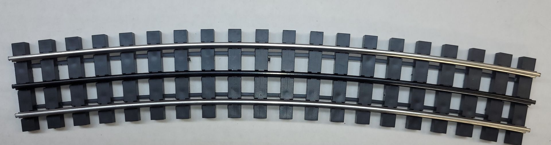 Curved model railroad track with gray rails and dark ties on a white surface