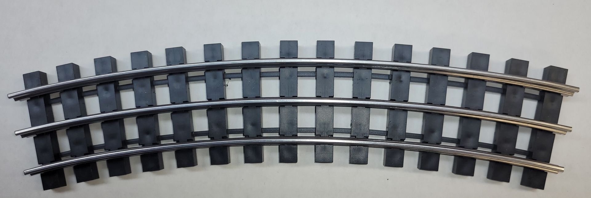 Curved model train track with dark rails and gray ties on a white background