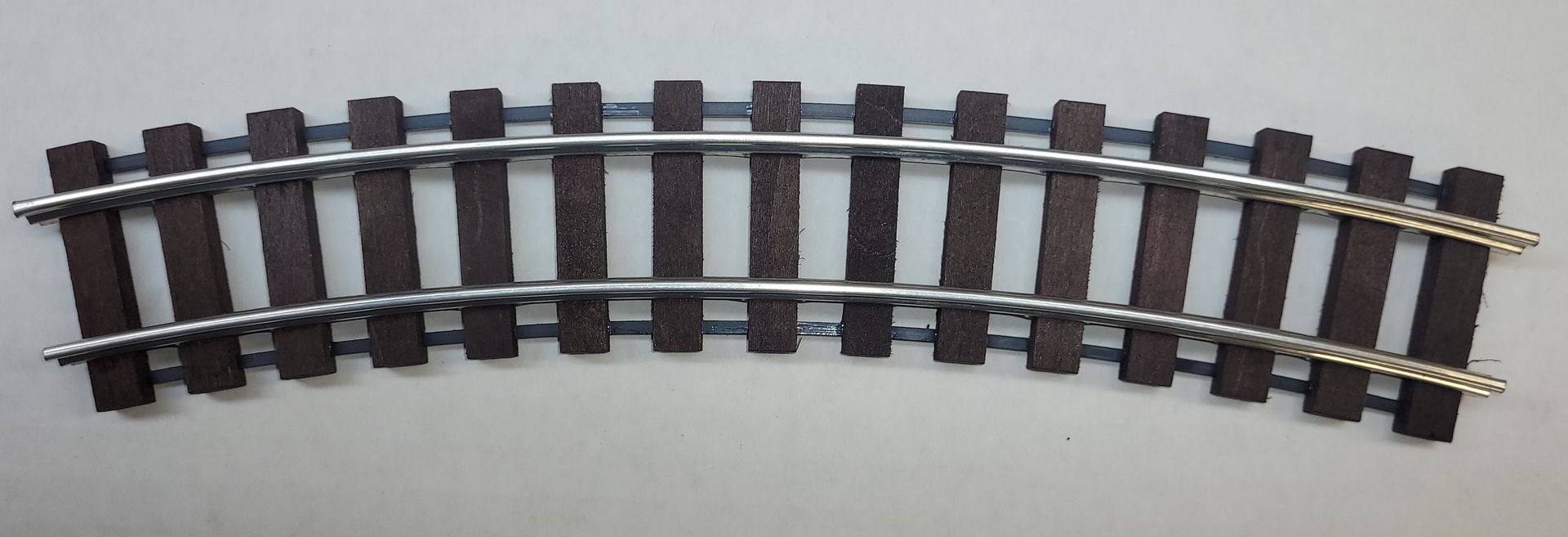Curved section of model train track with dark rails and brown ties on a light background