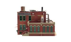 Red brick industrial building with green windows and rooftop pipes, viewed from the side.