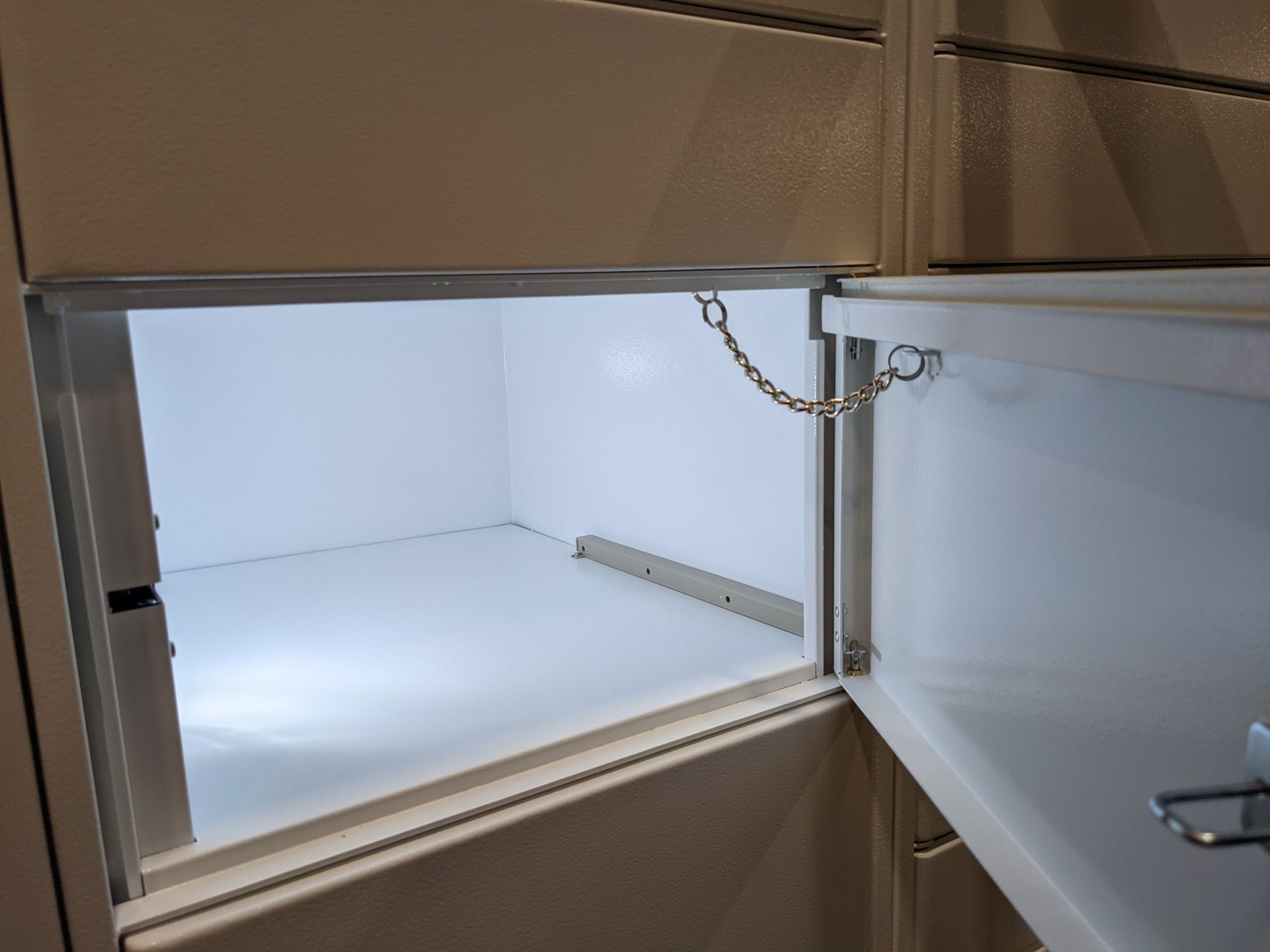 An open, empty white compartment with a safety chain, possibly a refrigerator or storage space.