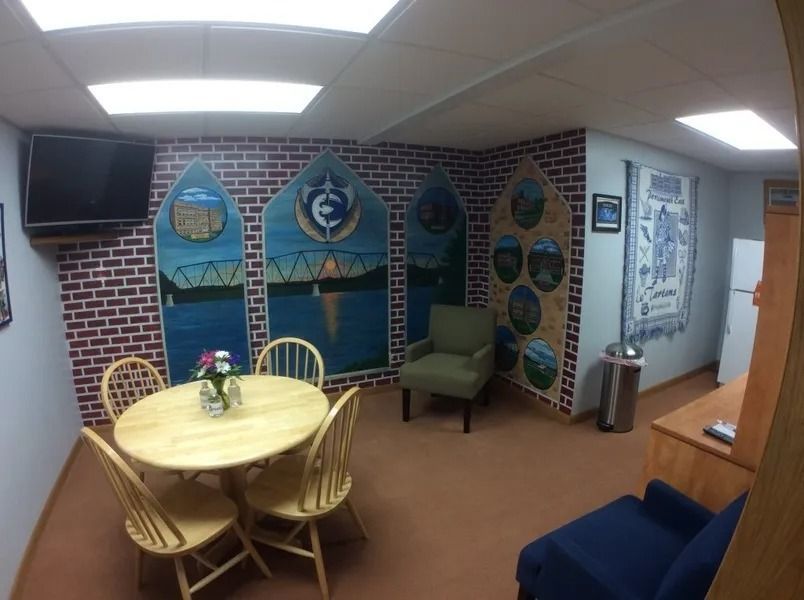 Small lounge with round table, chairs, brick wall decor, green armchair, TV, and hallway.