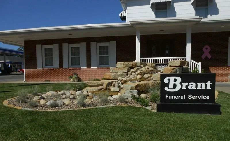 Brick funeral home with a Brant Funeral Service sign and pink ribbon in the front yard